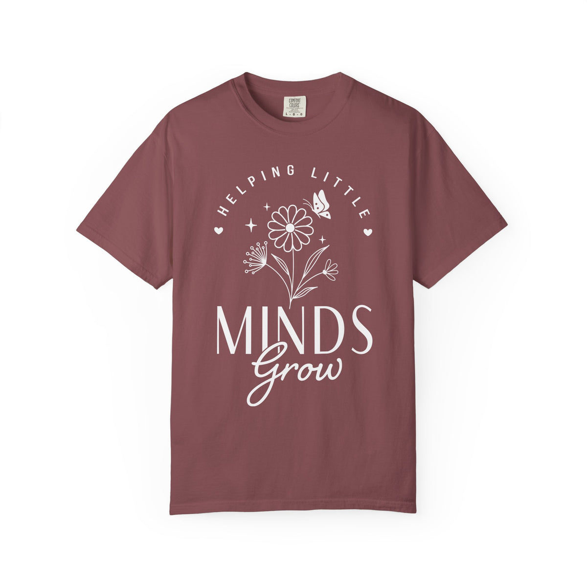 A short-sleeve crewneck t-shirt in a dusty mauve or burgundy color, featuring a white graphic print on the front with the text 'HELPING LITTLE MINDS Grow' and a flower illustration, displayed on a clean white background.