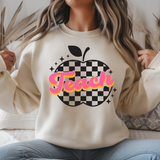 Person wearing a beige sweatshirt with 'Teach' and an apple graphic.