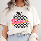 Person wearing a white t-shirt with 'Teach' and an apple graphic on a plain background
