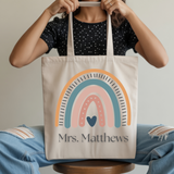 Person holding a tote bag with a rainbow design and 'Mrs. Matthews' text.
