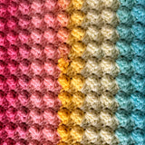 Close-up of a colorful crocheted fabric with pink, yellow, beige, and blue patterns.