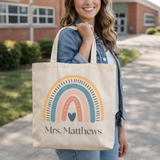 Woman holding a tote bag with a rainbow design and 'Mrs. Matthews' text.