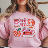Person wearing a pink sweatshirt with various graphics including a coffee cup, apple, and books.