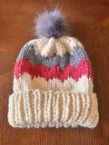 Knitted hat with colorful pattern and pom-pom on a wooden surface