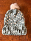 Knitted gray beanie with a white pom-pom on a wooden surface