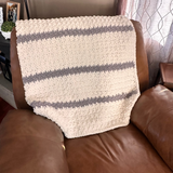Textured blanket draped over a brown leather sofa in a living room setting.