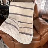 Textured blanket draped over a brown leather sofa in a living room setting.