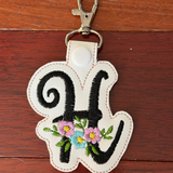Keychain with letter 'H' and floral design on a wooden surface