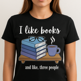 Person wearing a black t-shirt with a graphic of books, glasses, and a mug with text 'I like books and like, three people'.
