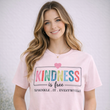 Woman wearing a pink t-shirt with 'Kindness is free' text, standing against a plain background.