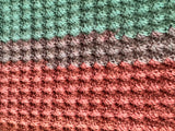 Close-up of a crocheted fabric with horizontal stripes in green, brown, and pink.