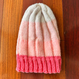 Knitted beanie with pink and white gradient on a wooden floor