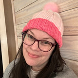 Person wearing a pink knit beanie and glasses on a wooden floor.