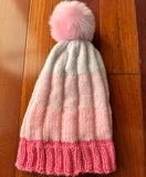 Knitted hat with pink trim and pom-pom on a wooden surface