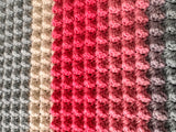 Close-up of a crocheted fabric with pink, gray, and beige stripes.