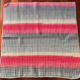 Striped blanket with red, gray, and beige colors on a wooden surface