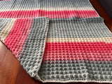 Crocheted blanket with pink and gray stripes on a wooden surface