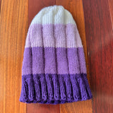 Knitted beanie with purple and white stripes on a wooden floor