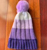 Knitted beanie with a purple pom-pom on a wooden floor