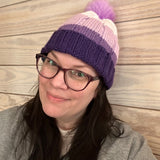 Person wearing a purple knit hat with a pink pom-pom on a wooden floor