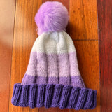 Knitted hat with purple brim and pink pom-pom on a wooden floor