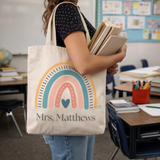 Person holding a tote bag with rainbow design and 'Mrs. Matthews' text in a classroom setting