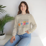 Woman wearing a beige sweatshirt with colorful text, sitting on a white surface with a plant in the background.