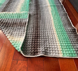 Knitted blanket with green and gray pattern on a wooden floor