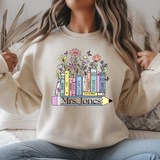 Person wearing a beige sweatshirt with colorful book design and 'Mrs. Jones' text.