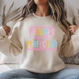 Person wearing a white sweatshirt with 'Progress Over Perfection' text in colorful letters.