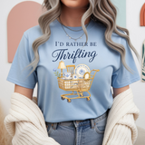 Person wearing a light blue t-shirt with a graphic and text 'I'd Rather Be Thrifting' in a casual setting.